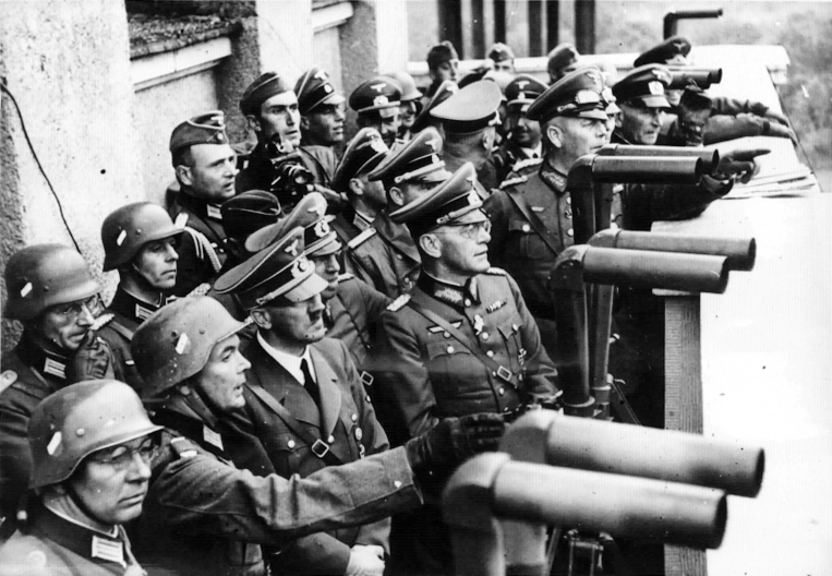 Adolf Hitler on a balcony crowded with military officers where several pairs of Scherenfernrohr are set up to view the siege of Warsaw